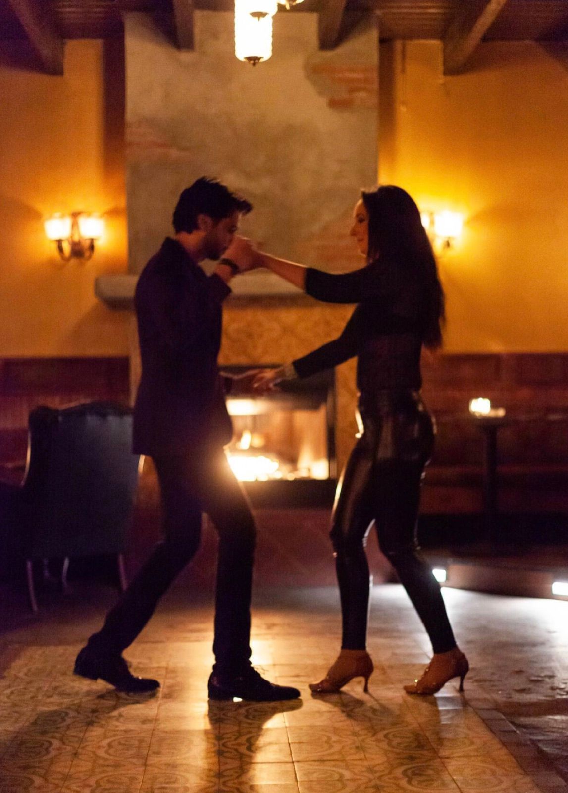 A couple dancing bachata beside a candlelit fireplace on a date night in Los Angeles