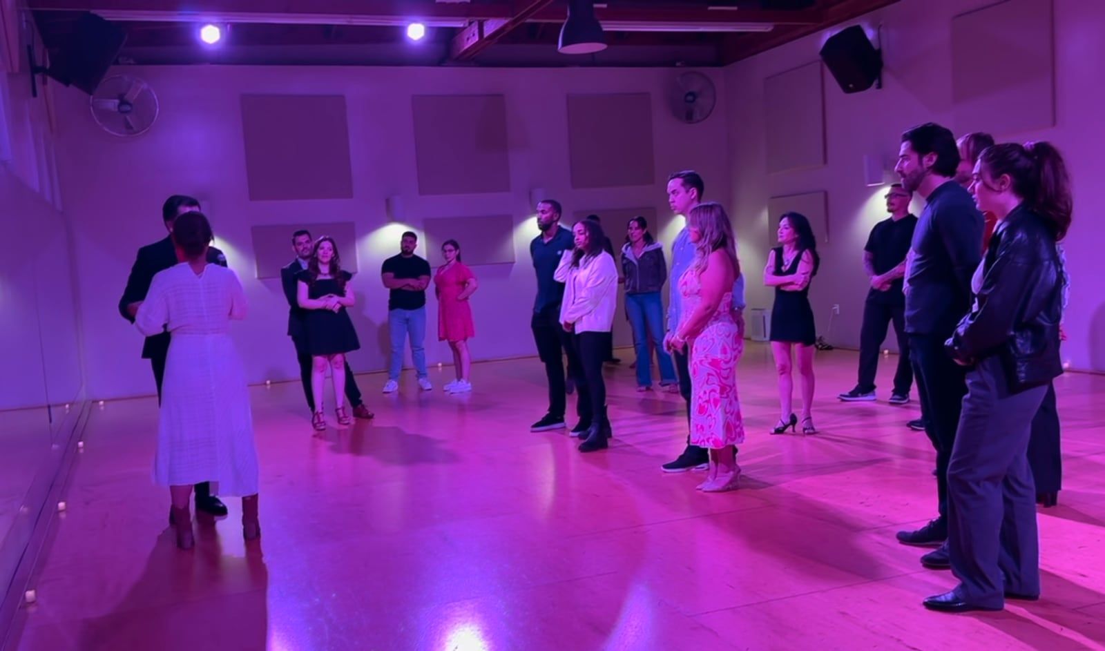 Students standing in a circle for a salsa workshop in a purple-lit Los Angeles studio