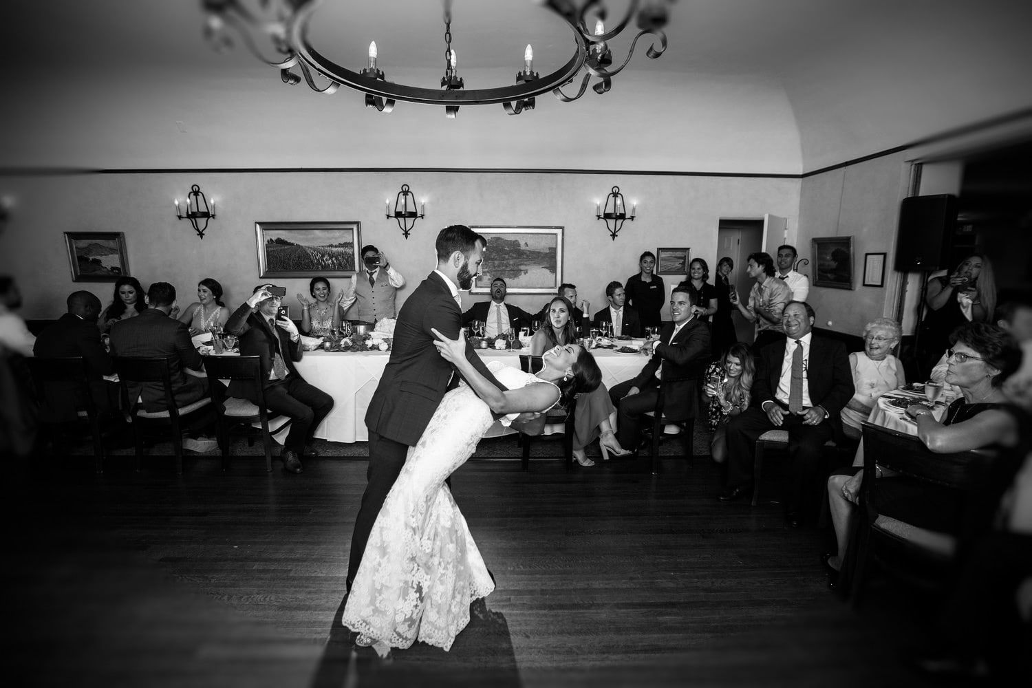 A groom dipping his bride during their first dance in a chandeliered ballroom