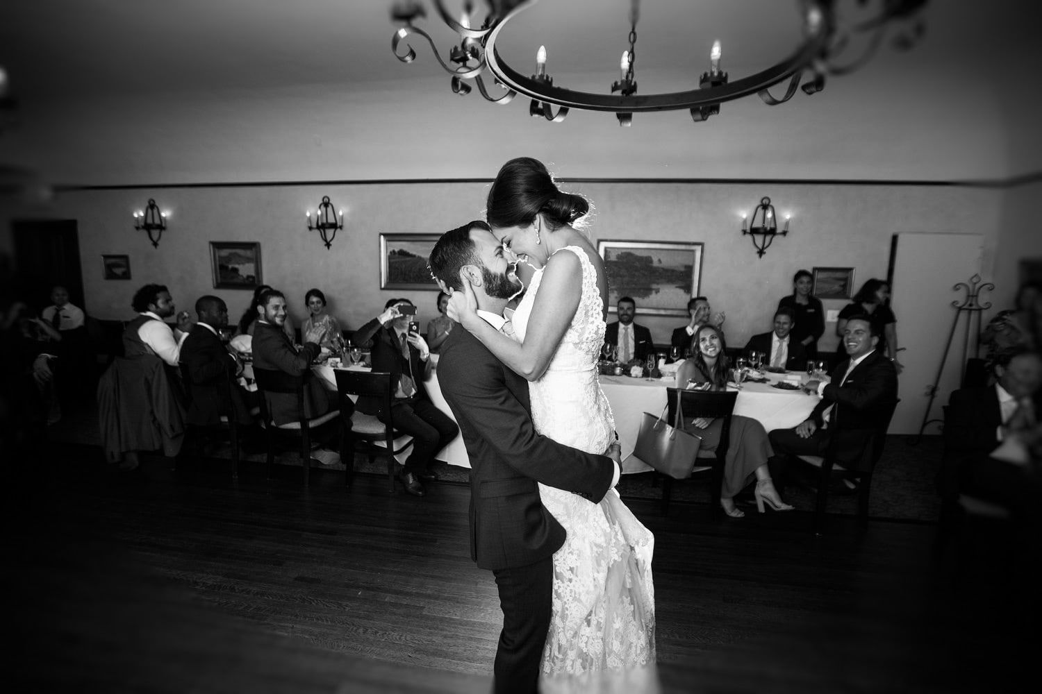 A bride and groom embracing at the end of their first dance, guests seated around the floor